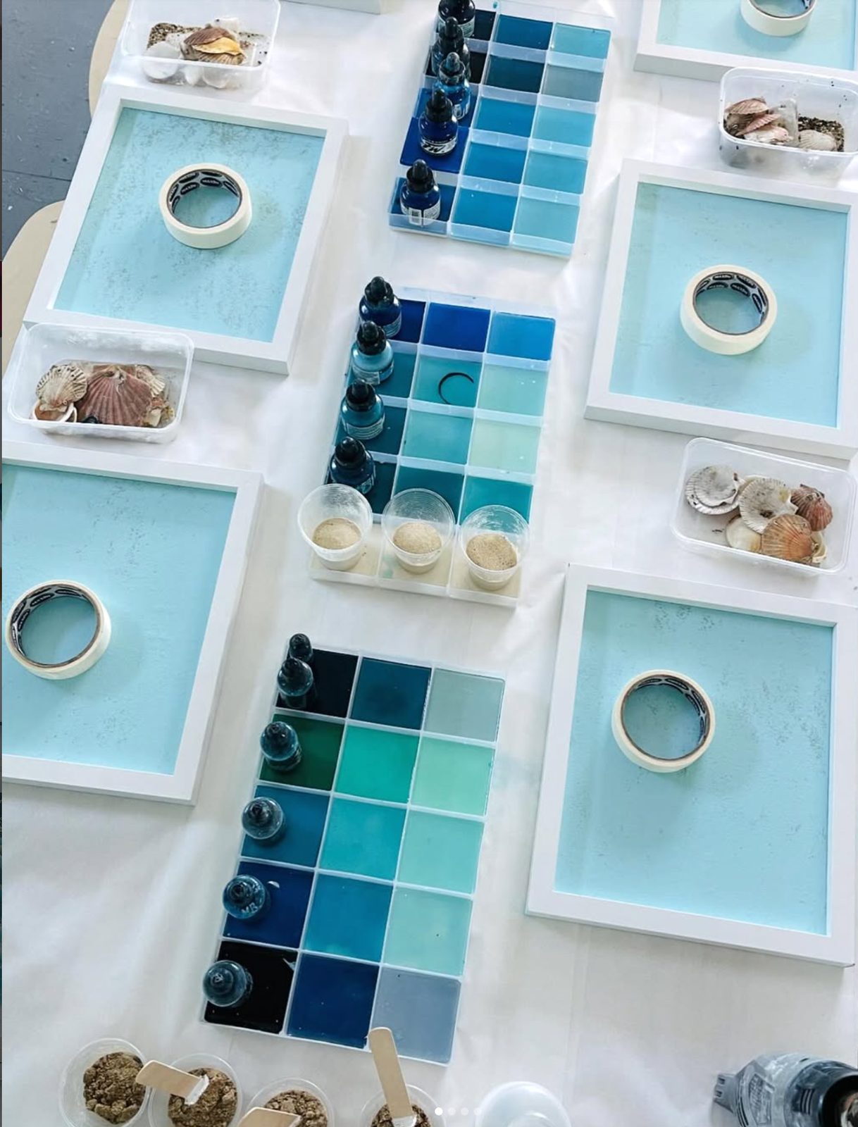 The workshop benches set for a session — white trays, shells and graded blue pigment palettes laid out for each guest.